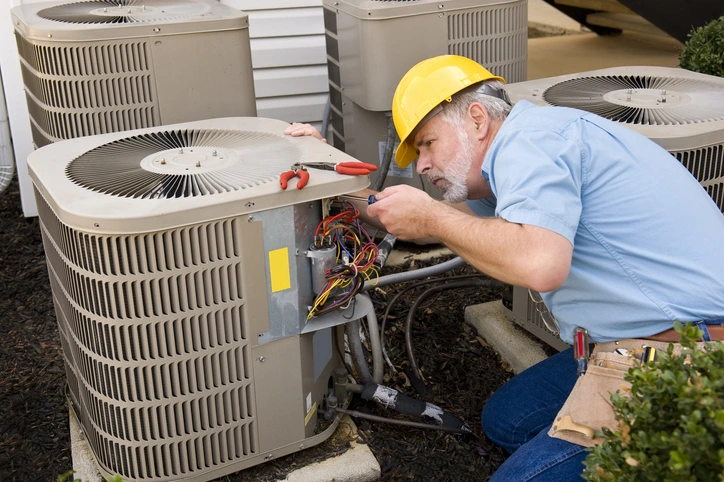 A man in a hard hat repairs an air conditioner, demonstrating skilled labor and safety in a maintenance setting.